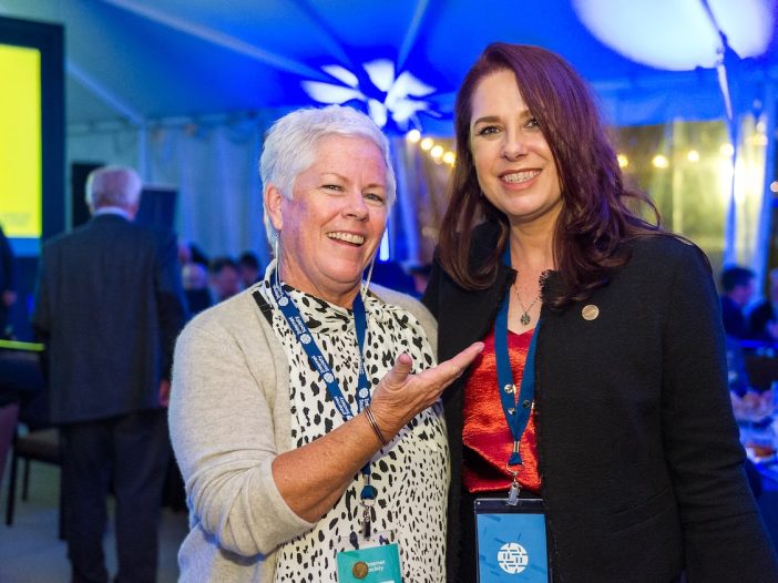 two women smiling while one is pointing to another with a hand